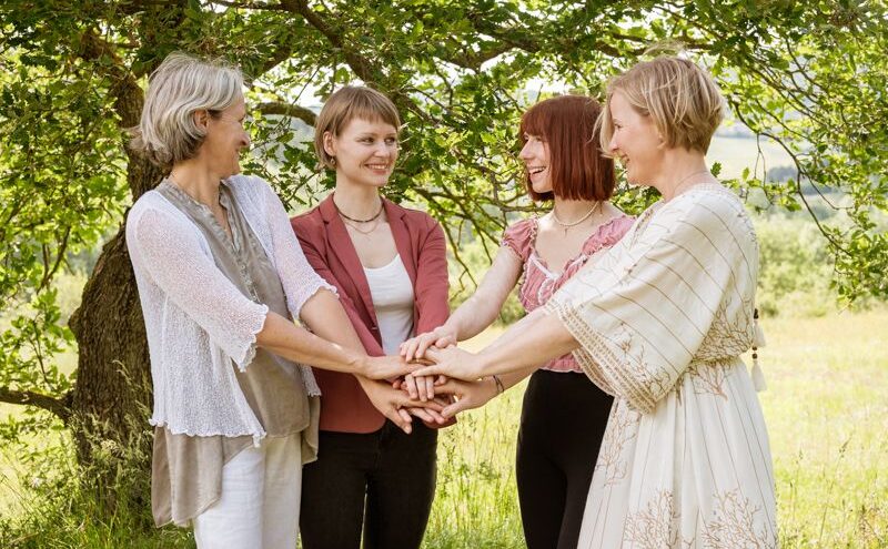 Das Team vom Holistic Life Home steht in der Natur und alle haben die Hände in der Mitte übereinander gestapelt und schauen sich dabei an.