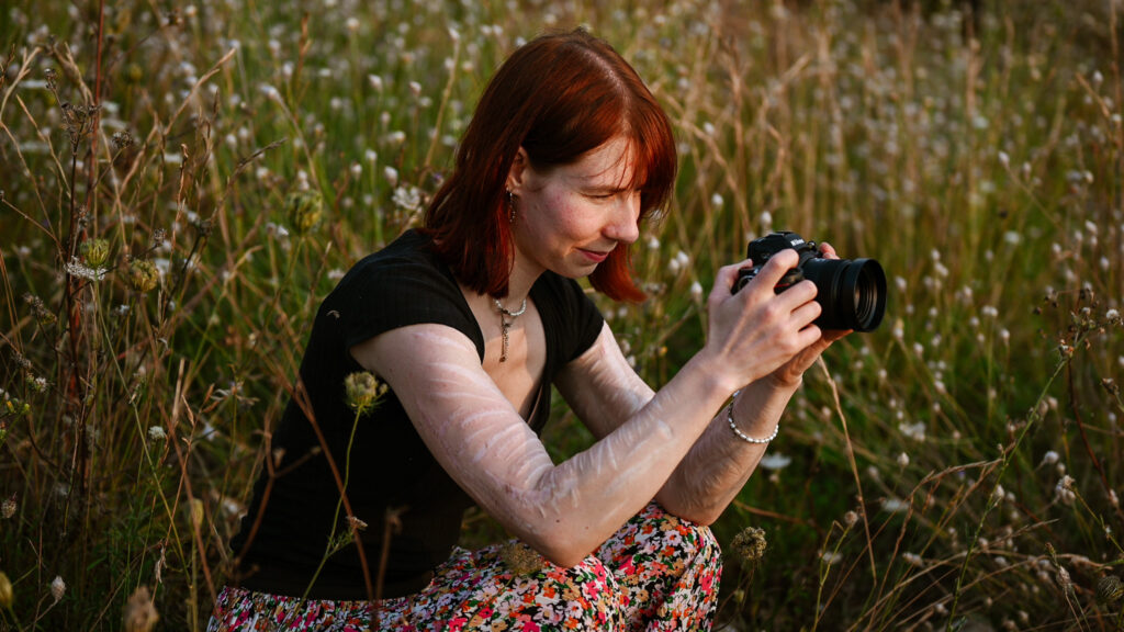 La'inesh hockt im Gras und macht mit einer Nikon Z5 Fotos von der Landschaft.