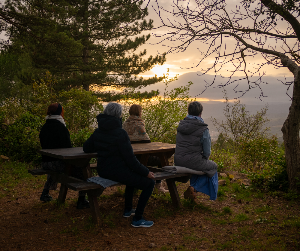 Das Team vom Holistic Life Home sitzt auf einer Picknickbank und meditiert bei Sonnenuntergang.