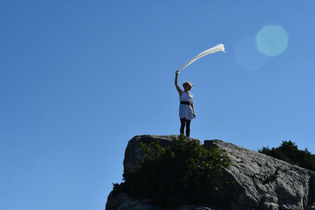 Frau steht mit einem Tuch auf einem Hohen Berg.