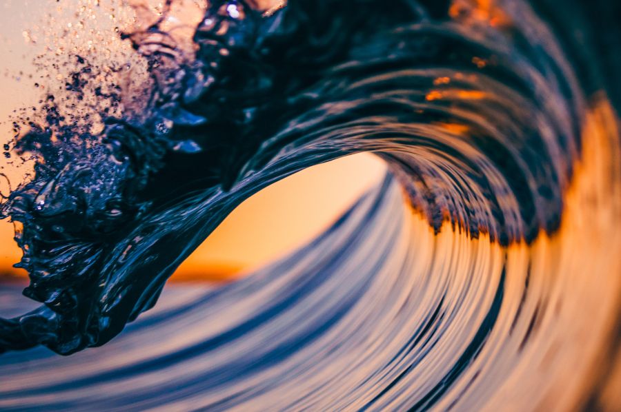 Eine große Welle, die sich gerade einrollt, in einem orange, blauem Licht.